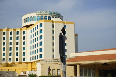 Khor Fakkan, Sharjah, Birleşik Arap Emirlikleri - 18 Nisan 2023: Bir Corvus görkemli kuşu arka planda Khor Fakkan 'daki Oceanic Khorfakkan Resort ve Spa binası ile bir trafik levhasında duruyor.