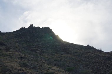 Güneş bulutlu bir gökyüzünde Nisan 'da Khor Fakkan, Sharjah, Birleşik Arap Emirlikleri' nde bir dağın arkasında batıyor.. 