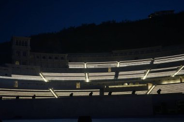 Nisan ayında akşam aydınlatmalı Khor Fakkan Amfitiyatrosu manzarası. Khor Fakkan Amfitiyatrosu, Khor Fakkan 'da yer alan bir açık hava tiyatrosudur. Rughaylat Yolu, Al Mudeife 1 