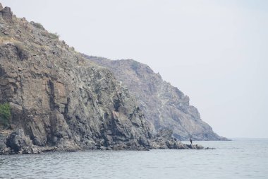 Khor Fakkan, Sharjah, BAE - 23 Nisan 2023: Elinde olta olan bir balıkçı Umman Körfezi 'nin kayalık kıyısında duruyor ve Nisan ayında Khor Fakkan' da balık tutuyor.                              