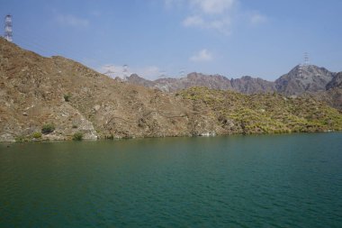 Nisan ayında El Rafisah Barajı 'nın dinlenme alanından dağlarla ve bitki örtüsüyle çevrili güzel Hawd al Bid' ah rezervuarının manzarası. Wadi Wshee, Sharjah, BAE. 