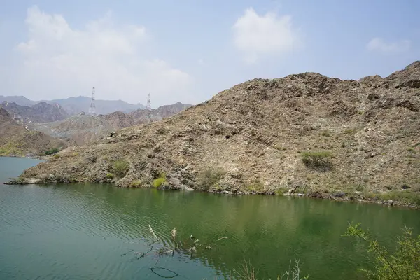 Nisan ayında El Rafisah Barajı 'nın dinlenme alanından dağlarla ve bitki örtüsüyle çevrili güzel Hawd al Bid' ah rezervuarının manzarası. Wadi Wshee, Sharjah, BAE. 