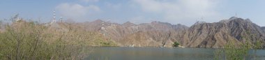Fotoğraf panoraması. Nisan ayında El Rafisah Barajı 'nın dinlenme alanından dağlarla ve bitki örtüsüyle çevrili güzel Hawd al Bid' ah rezervuarının manzarası. Wadi Wshee, Sharjah, BAE. 