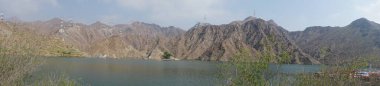 Fotoğraf panoraması. Nisan ayında El Rafisah Barajı 'nın dinlenme alanından dağlarla ve bitki örtüsüyle çevrili güzel Hawd al Bid' ah rezervuarının manzarası. Wadi Wshee, Sharjah, BAE. 