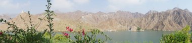 Fotoğraf panoraması. Nisan ayında El Rafisah Barajı 'nın dinlenme alanından dağlarla ve bitki örtüsüyle çevrili güzel Hawd al Bid' ah rezervuarının manzarası. Wadi Wshee, Sharjah, BAE. 