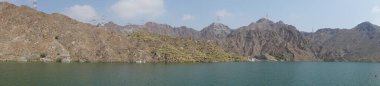 Fotoğraf panoraması. Nisan ayında El Rafisah Barajı 'nın dinlenme alanından dağlarla ve bitki örtüsüyle çevrili güzel Hawd al Bid' ah rezervuarının manzarası. Wadi Wshee, Sharjah, BAE. 