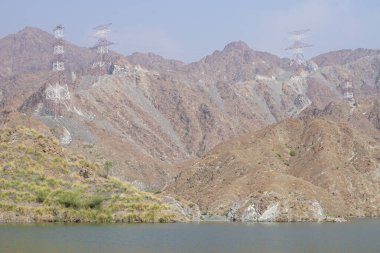 Hawd al Bid 'ah rezervuarının ve Nisan ayında El Rafisah Barajı' ndan çevresini çevreleyen dağların manzarası. Wadi Wshee, Sharjah, BAE.
