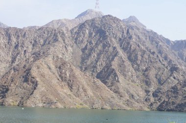 Hawd al Bid 'ah rezervuarının ve Nisan ayında El Rafisah Barajı' ndan çevresini çevreleyen dağların manzarası. Wadi Wshee, Sharjah, BAE.