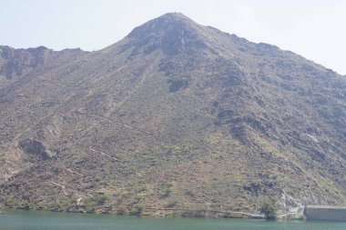 Hawd al Bid 'ah rezervuarının ve Nisan ayında El Rafisah Barajı' ndan çevresini çevreleyen dağların manzarası. Wadi Wshee, Sharjah, BAE.