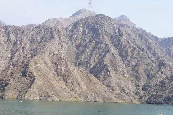 Hawd al Bid 'ah rezervuarının ve Nisan ayında El Rafisah Barajı' ndan çevresini çevreleyen dağların manzarası. Wadi Wshee, Sharjah, BAE.