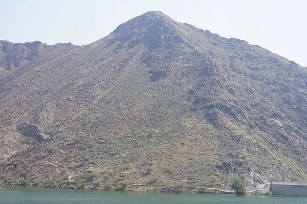 Hawd al Bid 'ah rezervuarının ve Nisan ayında El Rafisah Barajı' ndan çevresini çevreleyen dağların manzarası. Wadi Wshee, Sharjah, BAE.