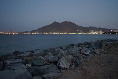 Nisan akşamı Umman Körfezi manzarası ve Khor Fakkan kenti kıyısı. Khor Fakkan, Birleşik Arap Emirlikleri 'nin doğu kıyısında, Şeriat Emirliği' ne bağlı bir şehirdir..                 