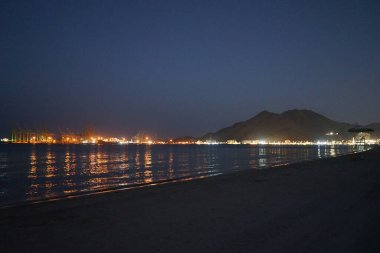 Nisan akşamı Umman Körfezi manzarası ve Khor Fakkan kenti kıyısı. Khor Fakkan, Birleşik Arap Emirlikleri 'nin doğu kıyısında, Şeriat Emirliği' ne bağlı bir şehirdir..                 