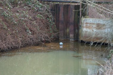 Şubat ayında Wuhlebecken veya Wuhlebecken nehri ile barajın yanındaki Wuhle Nehri 'nde mavi ve beyaz bir lastik top yüzer. Berlin, Almanya, Avrupa. 