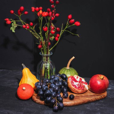 Siyah arka planda cam bir vazoda meyve ve gül ağacı dallarıyla dolu bir hayat. Şükran Günü konsepti Yakın çekim..