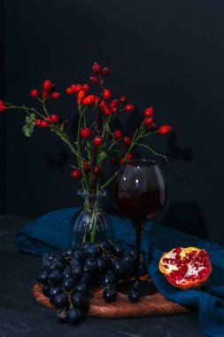 Üzüm, nar ve şarap kadehinde siyah arka planda içki. Durgun hayat. Seçici odak, yüzeysel alan derinliği.