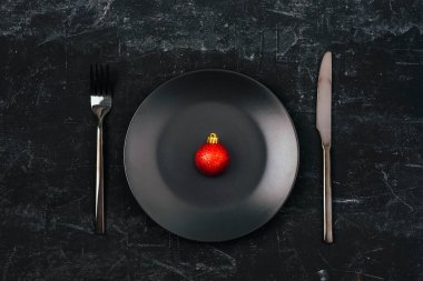 Noel sofrasında kırmızı Noel topu boş siyah tabakta ve siyah arka planda çatal bıçak takımı. Üst manzara, düz uzanma.