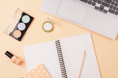 Defteri, dizüstü bilgisayarı, kalemi, makyaj malzemesi olan bir masaüstü. Güzellik blogcusu kavramı. Üst manzara, düz uzanma.