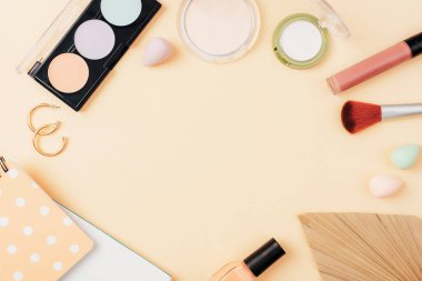 Kozmetik makyaj malzemesi ve bej arka planda not defteri ve palmiye yaprağından yapılmış çerçeve. Üst manzara, düz uzanma.