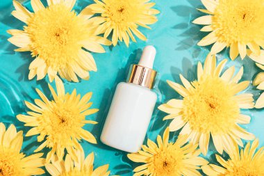 Beyaz kozmetik serum düşürücü şişe üzerinde sarı kasımpatı çiçekleri su kabarcıkları ile mavi su arka planında. Üst görünüm, düz görünüm, model.