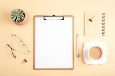 Boş dosya, not defteri, kahve fincanı ve açık bej arka planda aksesuarları olan bir masaüstü. Üst görünüm, düz görünüm, model.