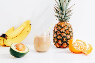Güneş ışığında beyaz ahşap masada meyveler, muz, ananas ve avokado kokteyli ile sakin bir hayat. Minimum detoks diyeti konsepti, yaz vitamini içeceği.