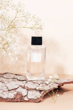 Ağaç kabuğunda boş etiketli parfüm şişesi ve tarafsız bej arka planda beyaz çingene çiçekleri. Ön görünüm.
