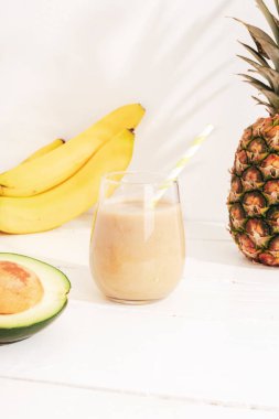 Muz, ananas ve avokado smoothie beyaz ahşap masa üzerinde güneş ışığında. Minimum detoks diyeti konsepti, yaz vitamini içeceği.
