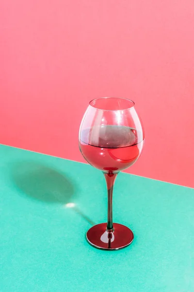 A glass of red wine on red and green background.