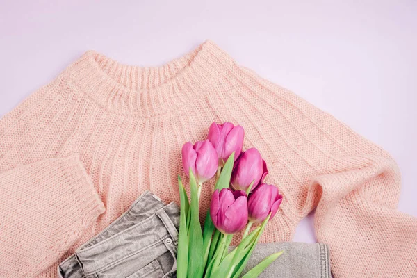 Bouquet of purple tulips on pink sweater and gray jeans. Casual clothes. Spring holidays concept. Top view, flat lay.