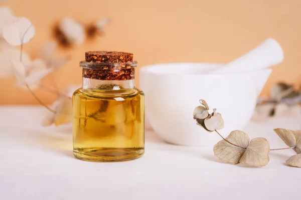 Cosmetic oil in glass bottle, mortar and pestle and eucalyptus branches on white table. Natural cosmetics, skincare, aromatherapy and beauty products. Closeup.