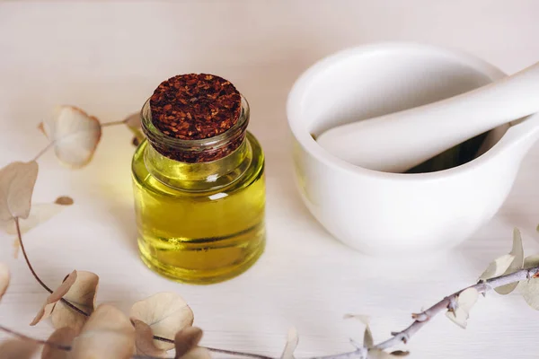 Cosmetic oil in glass bottle, mortar and pestle and eucalyptus branches on white table. Natural cosmetics, skincare, aromatherapy and beauty products. Top view.