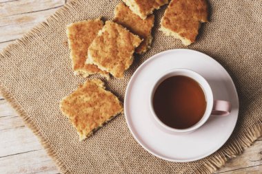 A cup of tea and homemade biscuits on sackcloth napkin on wooden table, top view.