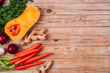 Raw butternut squash with carrot, red onion, ginger and garlic on wooden table. Pumpkin soup ingredients. Top view, flat lay, copy space.