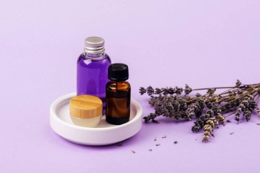 Lavender essential oil, serum and cream on white dish and dried lavender flowers. Skin care, aromatherapy, selfcare concept. Closeup.