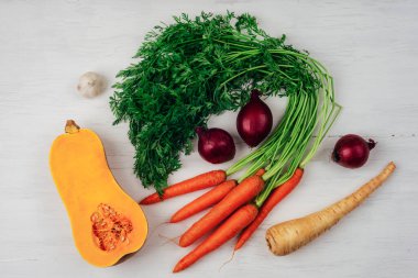 Carrot with greens, butternut squash, parsnip, garlic and onion on white wooden table. Healthy vegan food, harvest concept. Top view, flat lay.