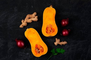 Raw butternut squash with red onion, ginger and parsley leaves on black background. Pumpkin soup ingredients. Top view, flat lay.