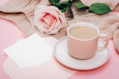 A coffee cup, pink rose and envelope with blank card. Holiday concept. Top view, mockup.