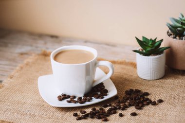 Coffee latte in white cup, coffee beans on sackcloth napkin. Closeup.