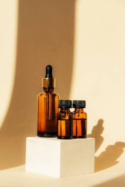 Natural essential oils and serum in brown glass bottle on a wooden podium. Alternative medicine, beauty skin care product. Copy space. Neutral background.