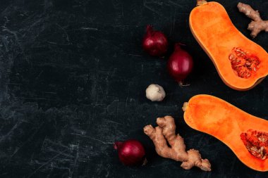 Raw butternut squash with red onion, ginger and garlic on black background. Pumpkin soup ingredients. Top view, flat lay, copy space.