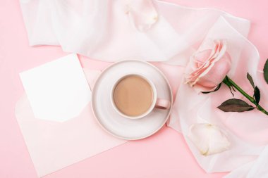 A coffee cup, pink rose and envelope with blank card. Holiday concept. Top view, flat lay, mockup.