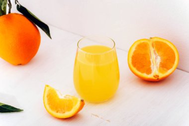 A glass of orange juice and orange fruits on white table. Closeup.