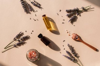 Lavender blossom, himalayan pink salt and essential oils on beige background with long shadows. Top view, flat lay.