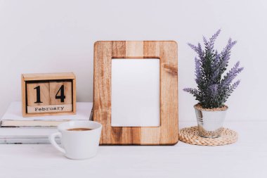 Sevgililer Günü tatil tarihli ahşap çerçeve ve blok takvimi. Kahve fincanı, çaydanlıkta çiçekler beyaz masada. Boşluğu kopyala.