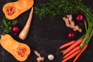 Frame of vegetables, pumpkin, carrot, ginger, onion, parsnip and parsley on black background. Healthy raw vegan food. Top view, flat lay, copy space.