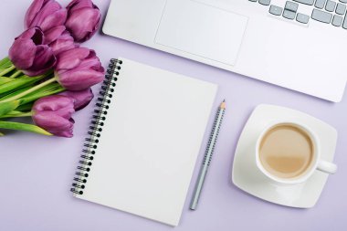 Blank notepad, laptop, pen, coffee cup and purple tulips on lilac background. Womens day, Mothers day concept. Top view, flat lay, mockup.