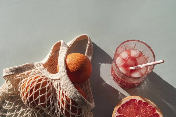 Fresh red grapefruit juice with ingredients and mesh bag in sunlight. Top view, flat lay.