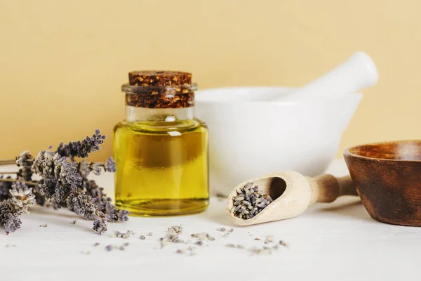 Natural cosmetic oil, white ceramic mortar and pestle and lavender dried flowers on white table. Natural cosmetics, skincare, aromatherapy and beauty products. Closeup.