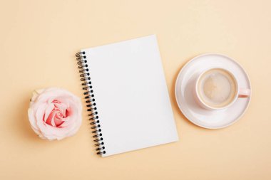 Coffee in cup, rose flower and spiral notebook on neutral background. Top view, flat lay, mockup.